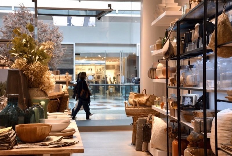 A bright shop with shelves of ceramics, baskets and wooden bowls opening onto a mall walkway