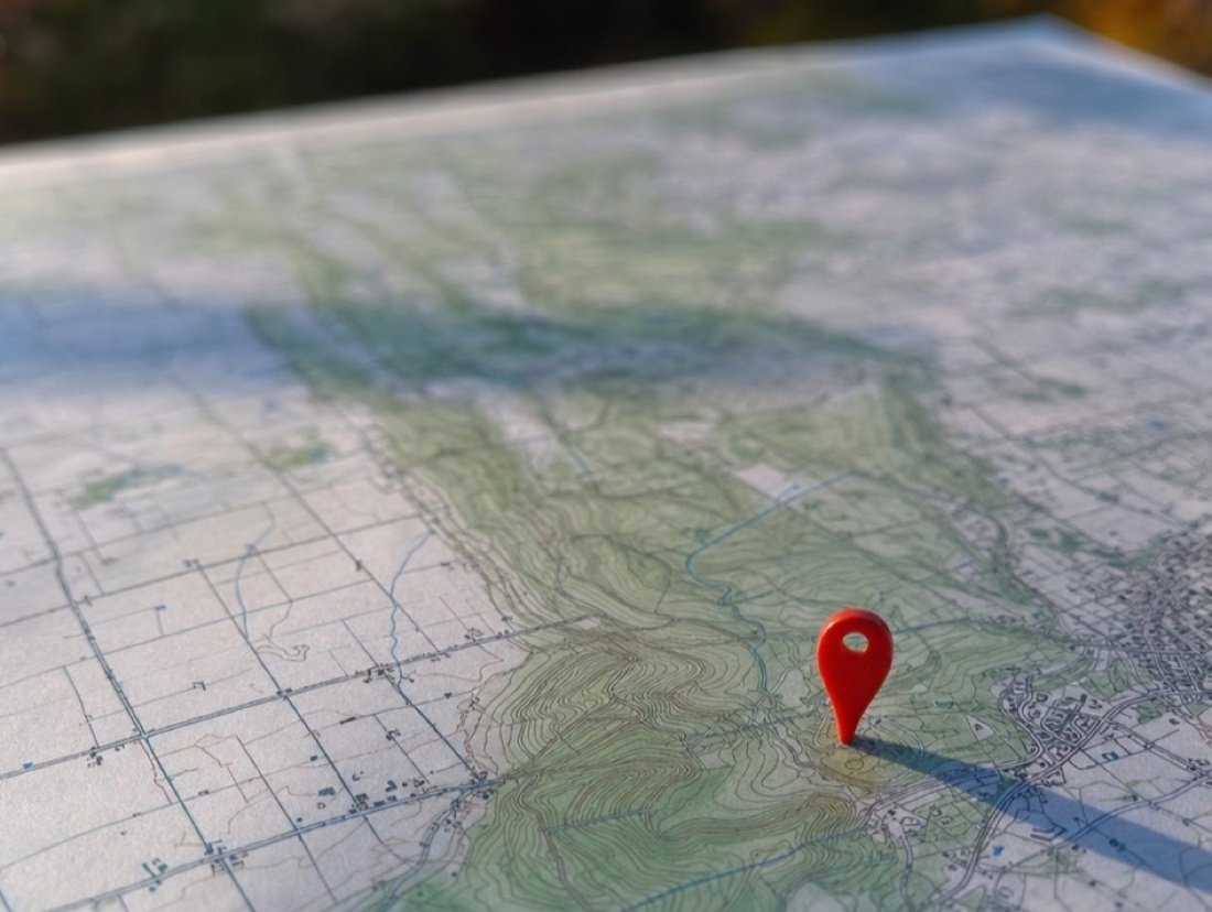 Close-up of a red pin pressed into the contour lines of a printed topographic map
