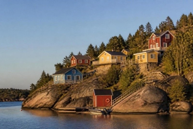 Colourful wooden houses on granite outcrops above a calm bay on a summer evening